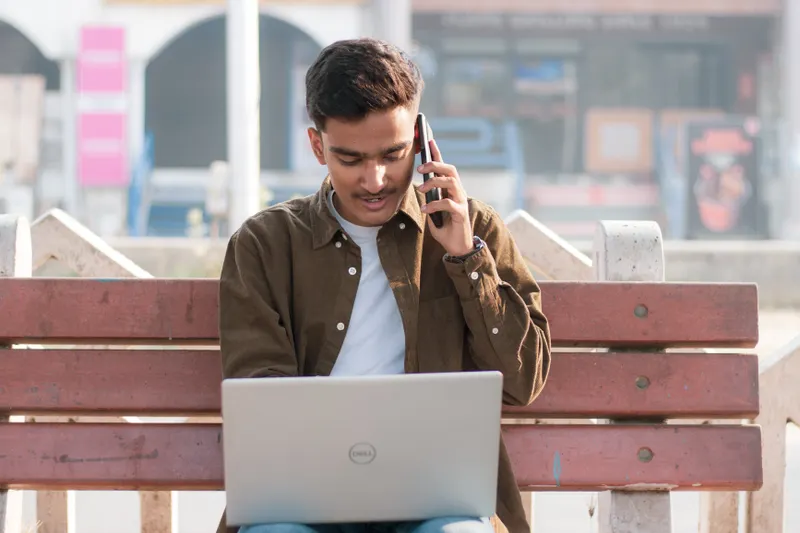 Young business owner on a phone call while working on a laptop outdoors