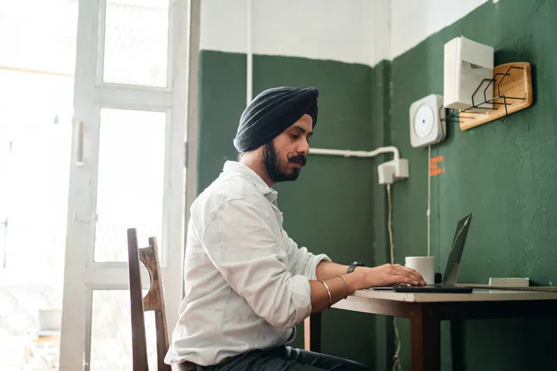 Professional in a turban typing on a laptop at a café table