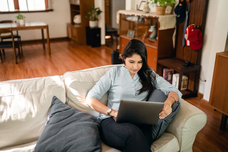 Woman working on a laptop while sitting on a sofa at home